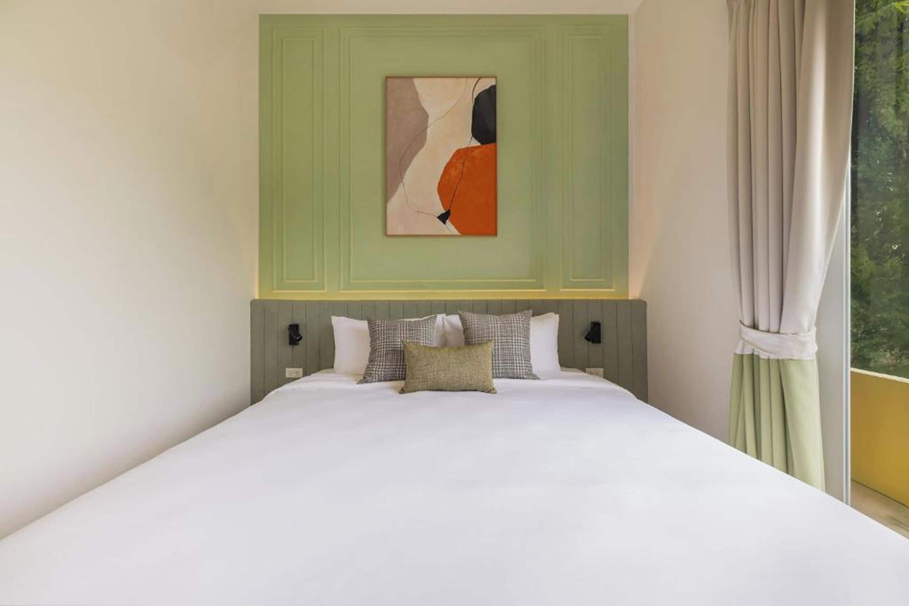 A bedroom with a bed, pillows, a painting, and a view through a window.