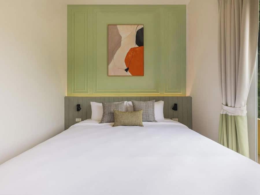 A bedroom with a bed, pillows, a painting, and a view through a window.