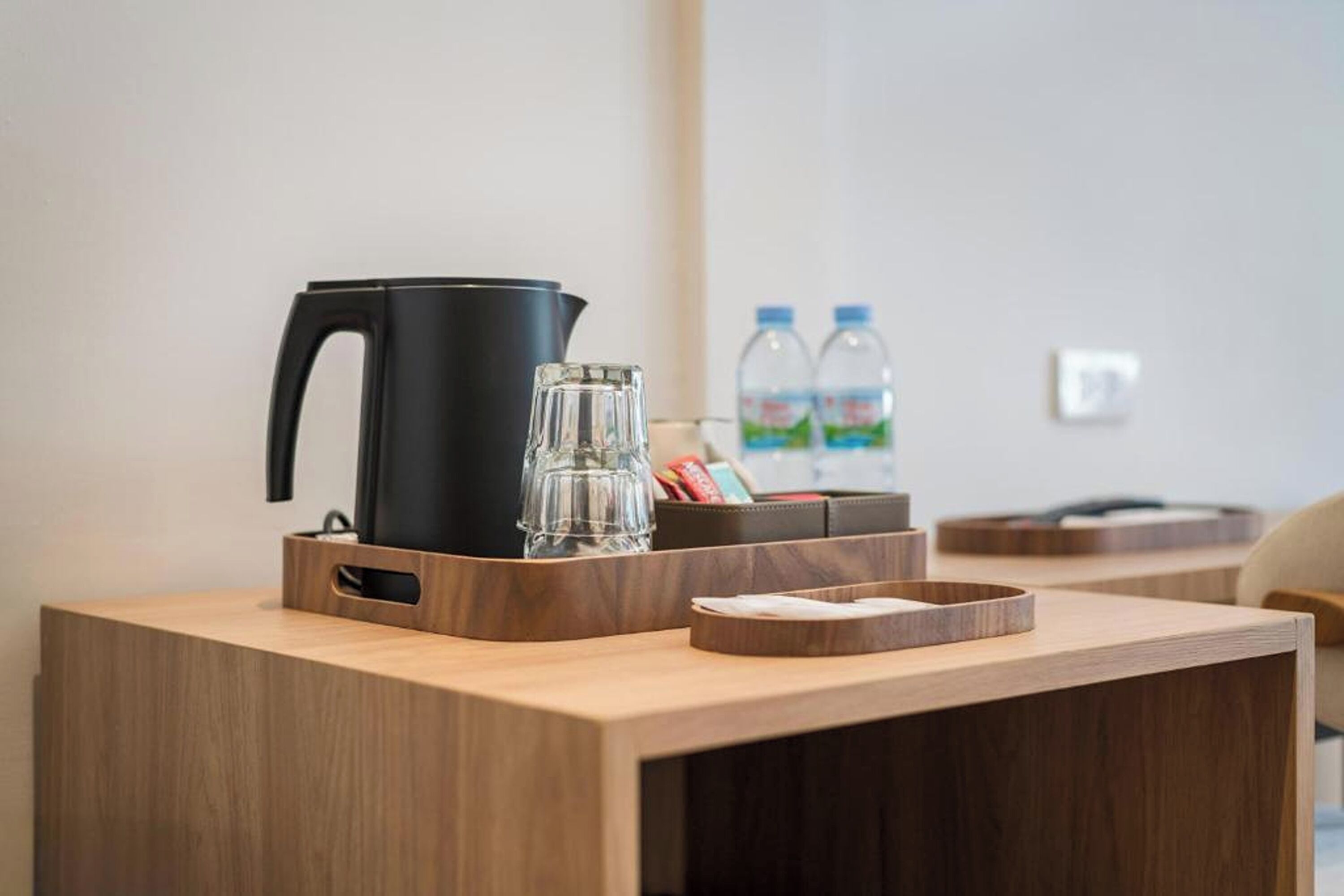 A wooden desk with a black kettle, a glass, and a tray with pens and a notebook.