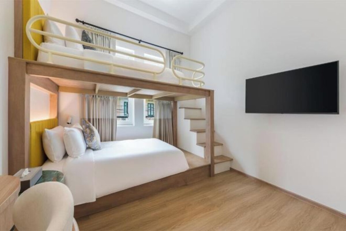 A bunk bed room with a TV mounted on the wall, a staircase, and a window with curtains.