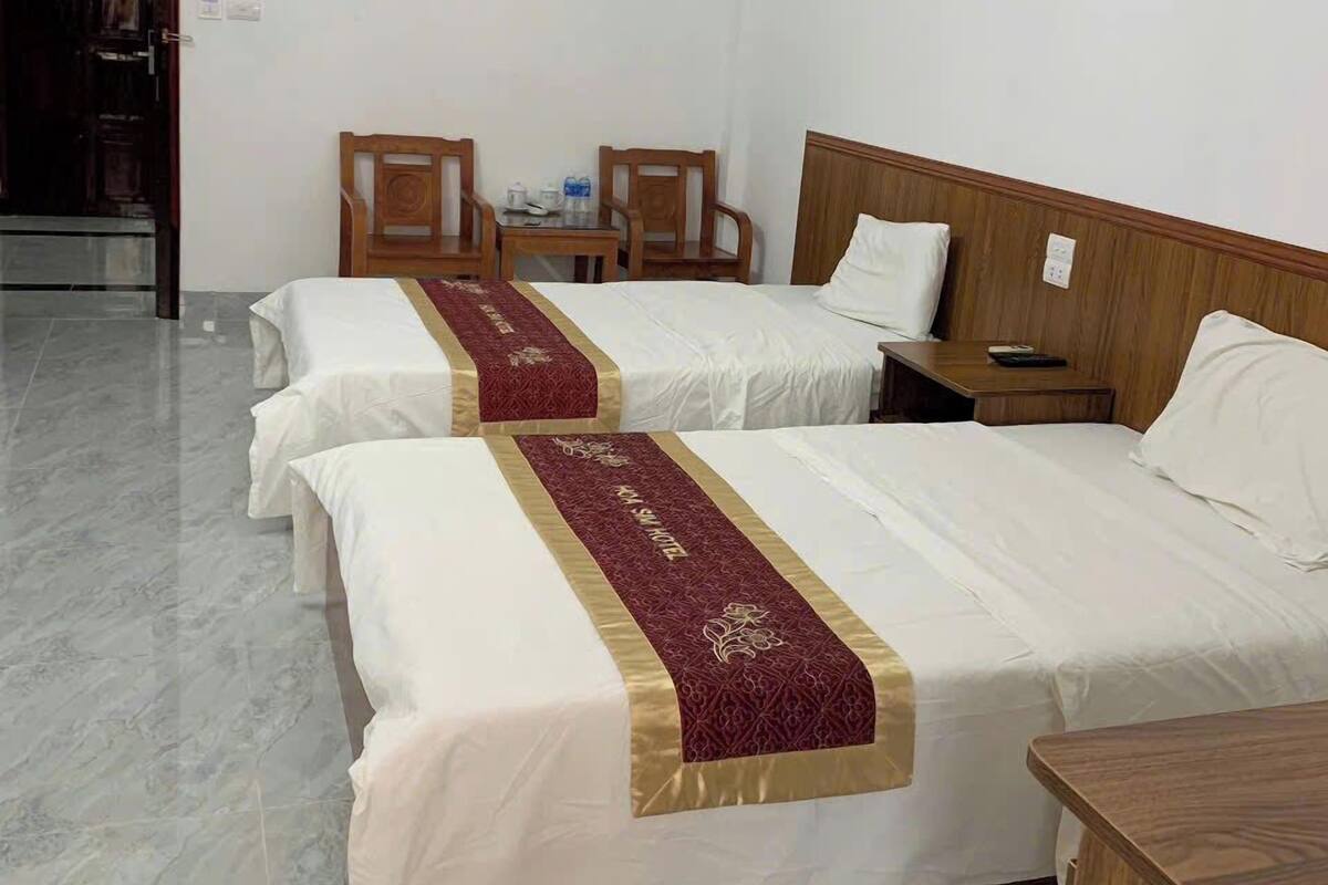 A hotel room with two beds, a wooden headboard, a small table with chairs, and a wardrobe.