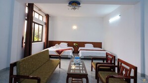A hotel room with two single beds, a wooden bench, a small table with water bottles, and a ceiling fan.