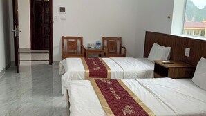 A hotel room with two beds, a wooden nightstand, a small table with chairs, and a window with a view of buildings.