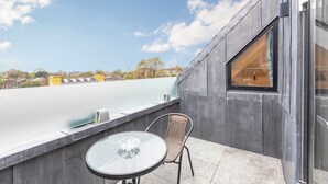 A balcony with a table and chair, overlooking a body of water and buildings.