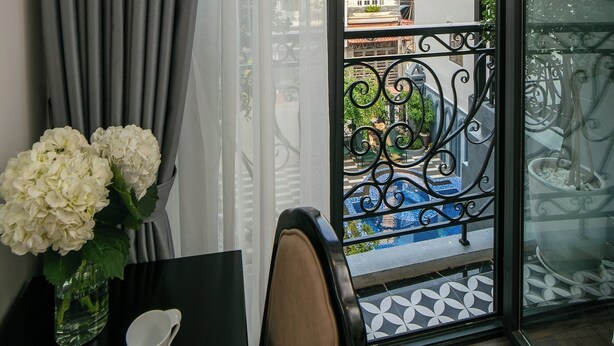 Un balcon donnant sur des immeubles et des arbres, une table avec un vase de fleurs et une chaise.