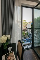 Un balcón con vistas a edificios y árboles, una mesa con un florero y una silla.