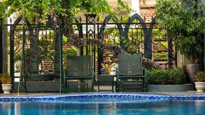 Un espace piscine bordé de carreaux, avec deux fauteuils en osier et un portail en fer forgé.