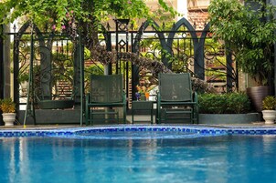 Zona de piscina con borde de azulejos, dos sillas de mimbre y una reja de hierro forjado.