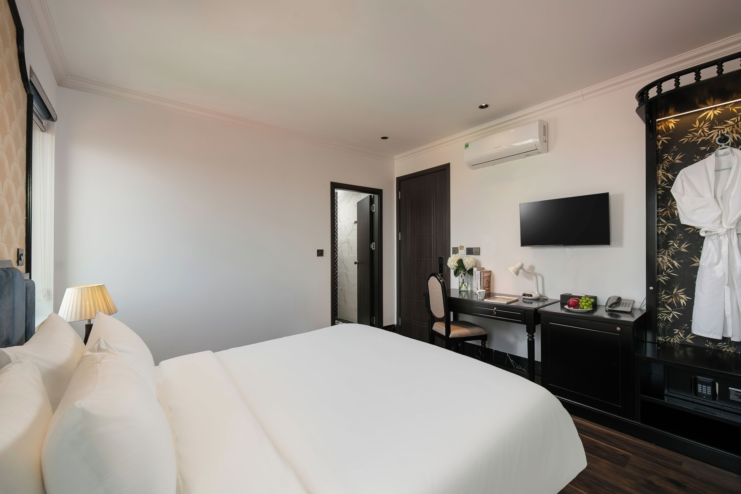 A hotel room with a large bed, a desk with a chair, a TV, a robe hanging on the wall, and a mirror.