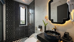 Une salle de bain moderne avec un mur orné d’un motif géométrique, un grand miroir, un lavabo avec un récipient bleu et des toilettes.
