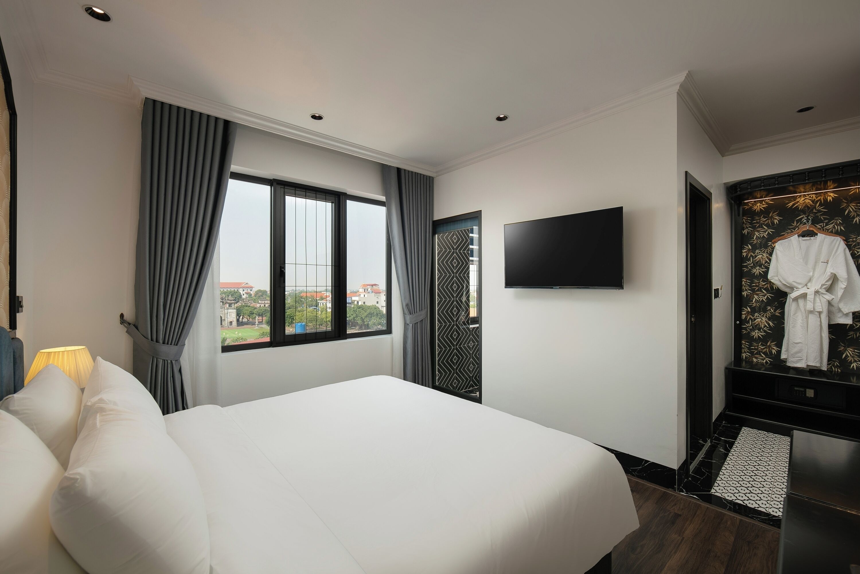 A hotel room with a large bed, a flat-screen TV mounted on the wall, a wardrobe with a mirror, and a window with curtains.