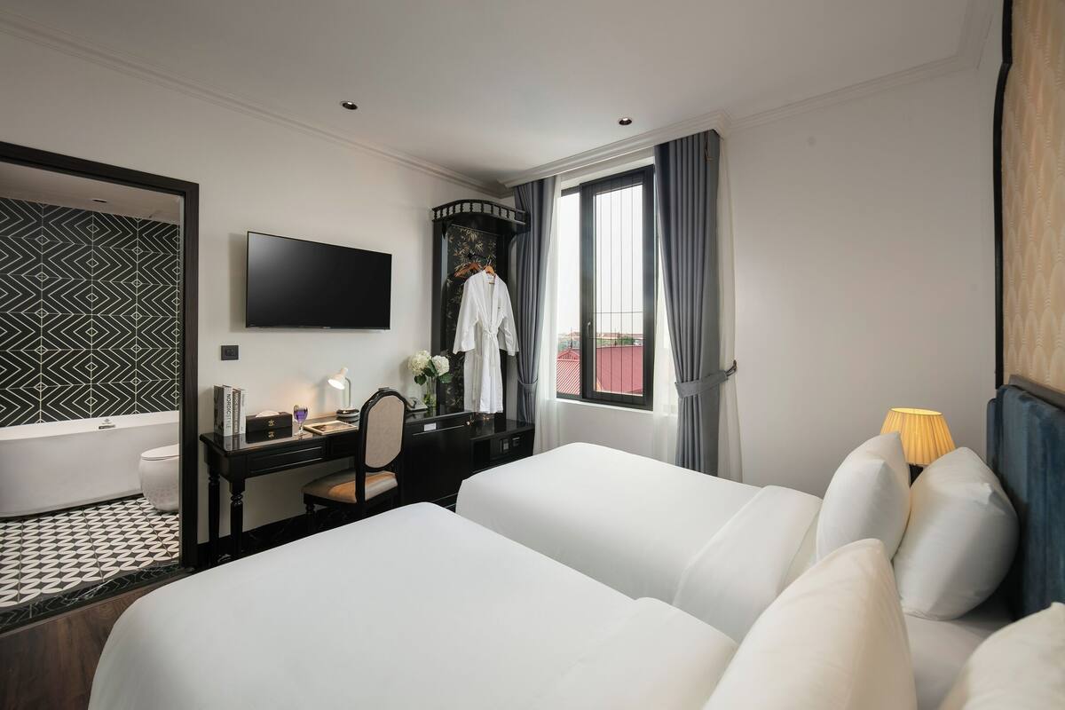 Une chambre d’hôtel avec un grand lit, un bureau avec une chaise, une télévision et une fenêtre avec des rideaux.