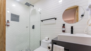 A modern bathroom with a glass shower enclosure, white herringbone-patterned tiles, a white toilet, a black sink with a round mirror, and a towel rack. - Comfortable Private Suite in Condesa area (18) (Mexico)