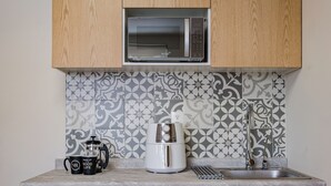 Una cocina con microondas, cafetera y máquina de espresso sobre la encimera, un lavabo y azulejos decorativos en la pared.