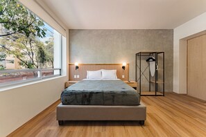 Ein modernes Schlafzimmer mit einem großen Bett, Holzboden, Blick ins Freie und einem eingebauten Kleiderschrank.