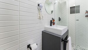 A modern bathroom with white tiled walls, a round mirror, a white sink, and a glass shower enclosure. - Comfortable Private Suite in Condesa area (18) (Mexico)