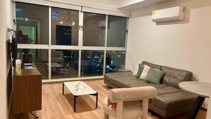 A modern living room with a sofa, a small table, and a chair. There is a large window with a view of the city at night. - Ph Quartier Boutique 16C apt with rooftop pool (Panamá)