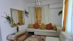 Una sala de estar con un sofá blanco, una mesita de madera, un espejo decorativo y una alfombra estampada.