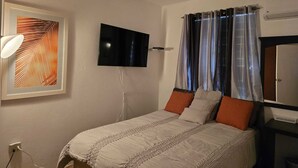 Un dormitorio con una cama, un televisor de pantalla plana en la pared, una obra de arte enmarcada y una ventana con cortinas.