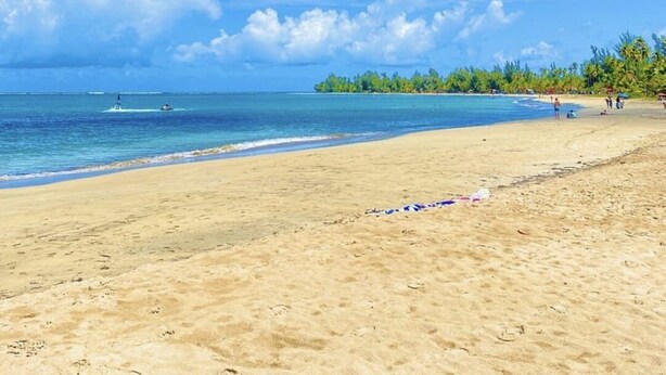 Una playa con aguas azules cristalinas, una orilla de arena y una isla lejana con palmeras.