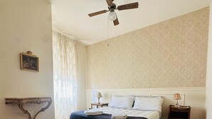 A bedroom with a wooden floor, a bed with white linens, a ceiling fan, and a small bedside table with a lamp. - Liguria - Galleria Goito La Spezia (La Spezia)