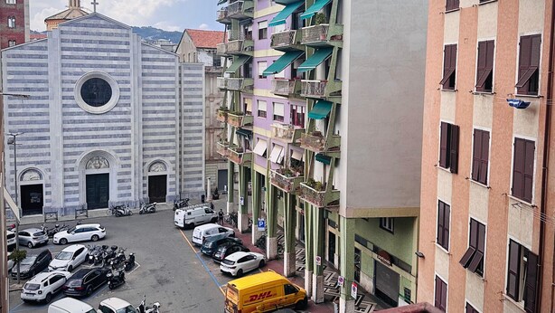 A multi-story building with balconies and a church in the background. - Liguria - Galleria Goito La Spezia (La Spezia)