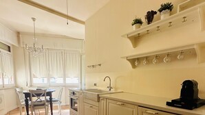 A kitchen with white cabinets, a sink, and a coffee maker. There is a dining area with a table and chairs. - Liguria - Galleria Goito La Spezia (La Spezia)