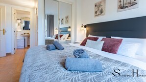 A hotel room with a large bed, a bathroom with a sink and mirror, and artwork on the walls. - Mountain Views, Pool & Rooftop: Cozy 2BR for 6 REF034 (Fuengirola)