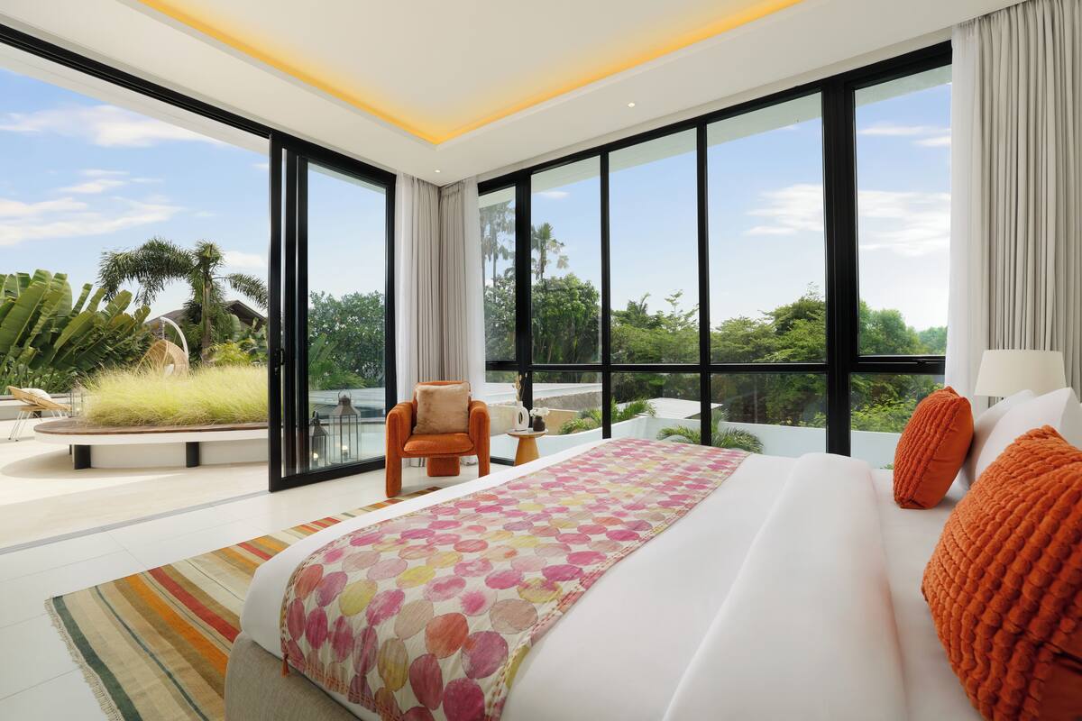 Una habitación de hotel moderna con una cama grande, vistas a zonas verdes y un balcón.