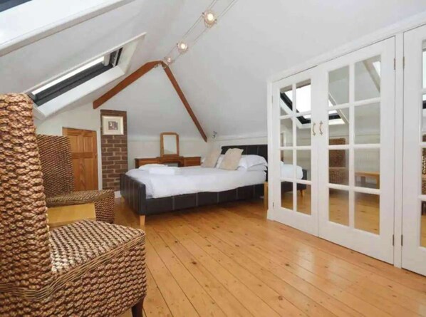 A bedroom with a sloped ceiling, a bed, a chair, and a wardrobe with glass doors.