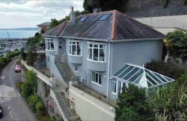 A two-story house with a sloped roof, a small front porch, and a garage. - 4 Bed House - Parking, Pets, Marina & Sea Views (Torquay)