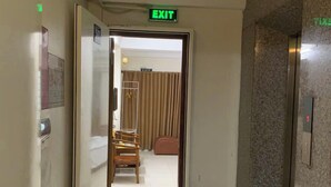 Un pasillo de hotel con una señal de salida, una silla de madera, una cama y un extintor.