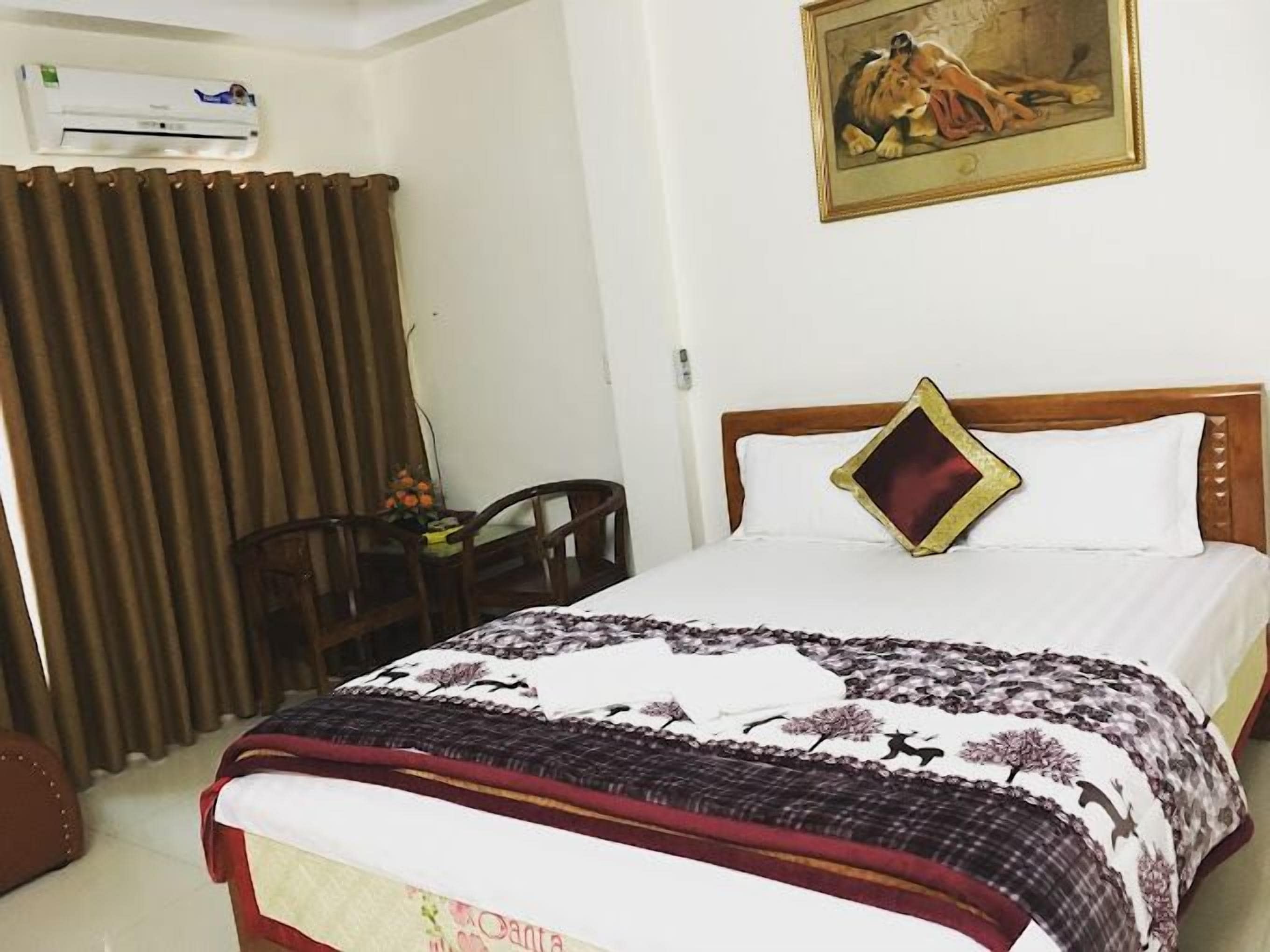 A hotel room with a bed, a desk, a chair, a window with curtains, and an air conditioning unit.