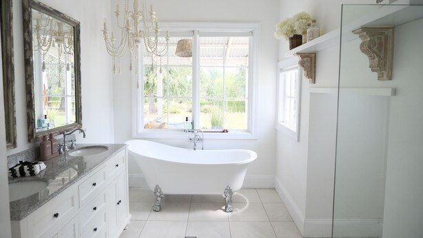 Une salle de bain avec une baignoire sur pieds, un grand miroir et un lustre.