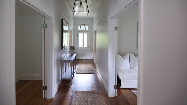 A hallway with a wooden floor, white walls, and a white sofa at the end.