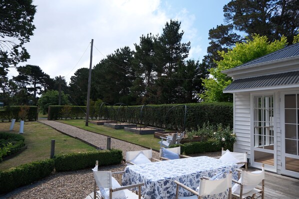 A patio area with a table and chairs, surrounded by a garden with hedges and trees. - Luxury farm stay just 12 minutes from Braidwood (Durran Durra)
