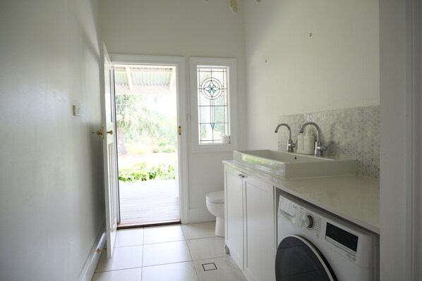 A compact, well-lit bathroom with a washing machine, a sink, and a toilet. - Luxury farm stay just 12 minutes from Braidwood (Durran Durra)