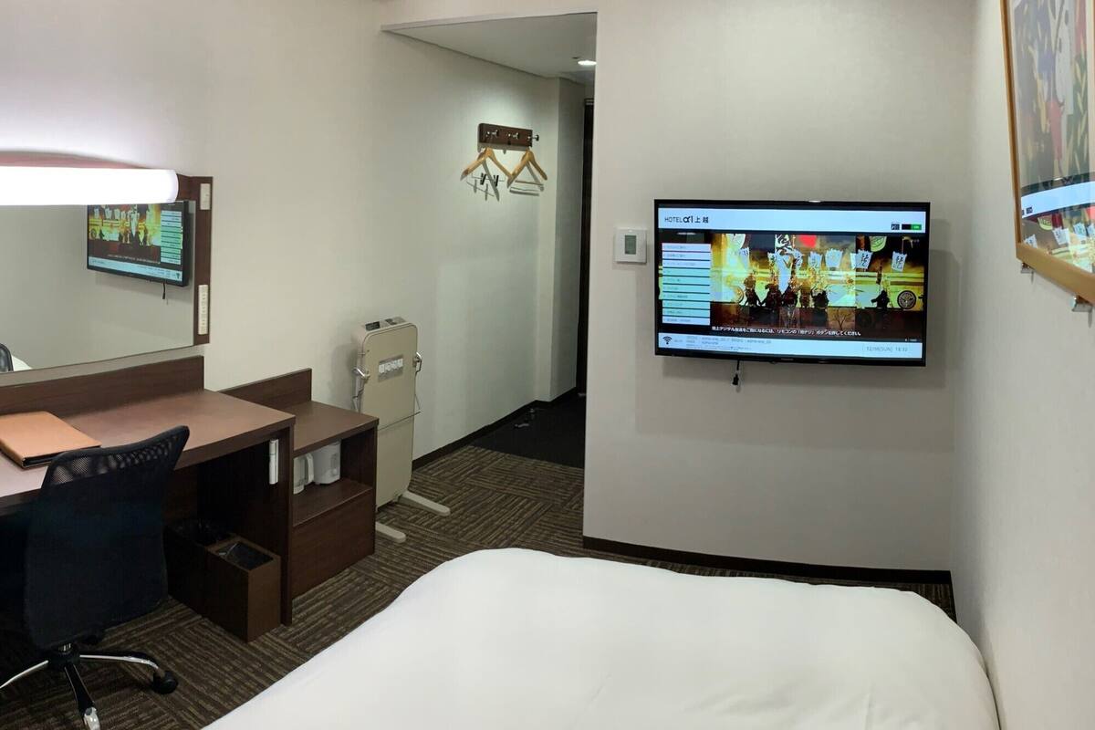 Ein Hotelzimmer mit Bett, Schreibtisch, Stuhl, Fernseher und einer Minibar.