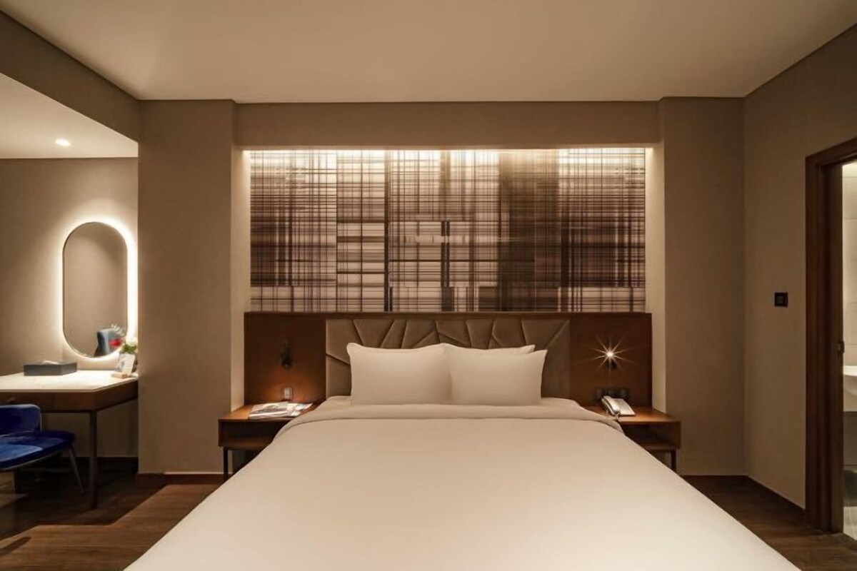 A modern hotel room with a large bed, a desk with a chair, and a nightstand with a phone.