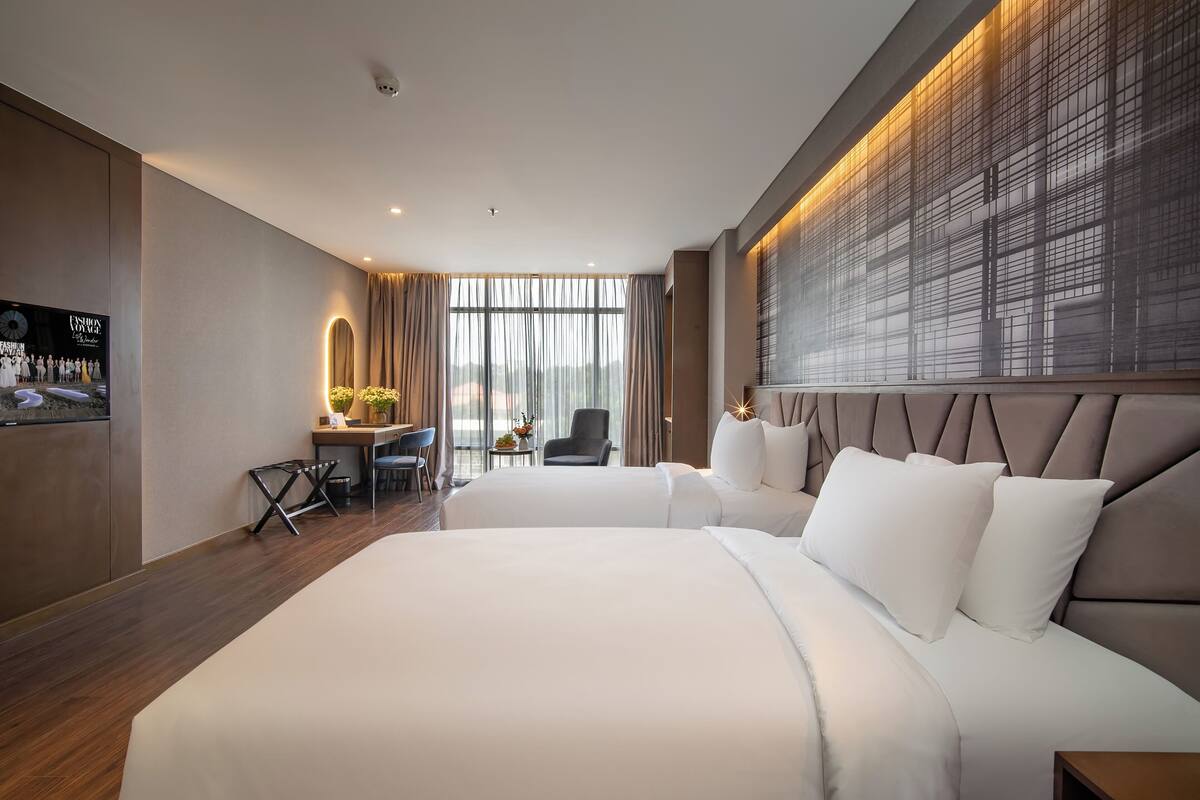 A hotel room with two large beds, a desk with a chair, and a large window with curtains.