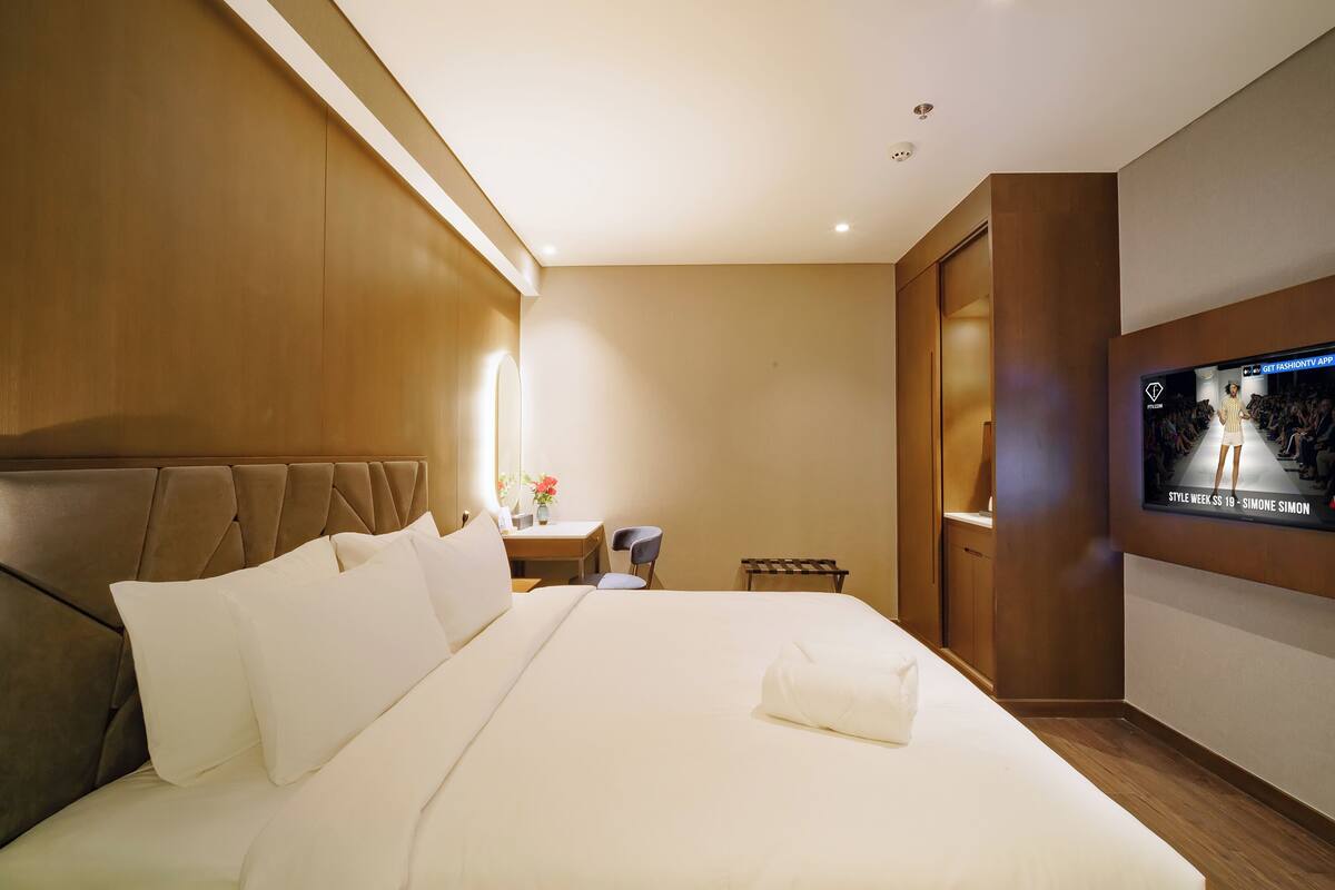 A hotel room with a large bed, a desk, a chair, and a TV mounted on the wall.