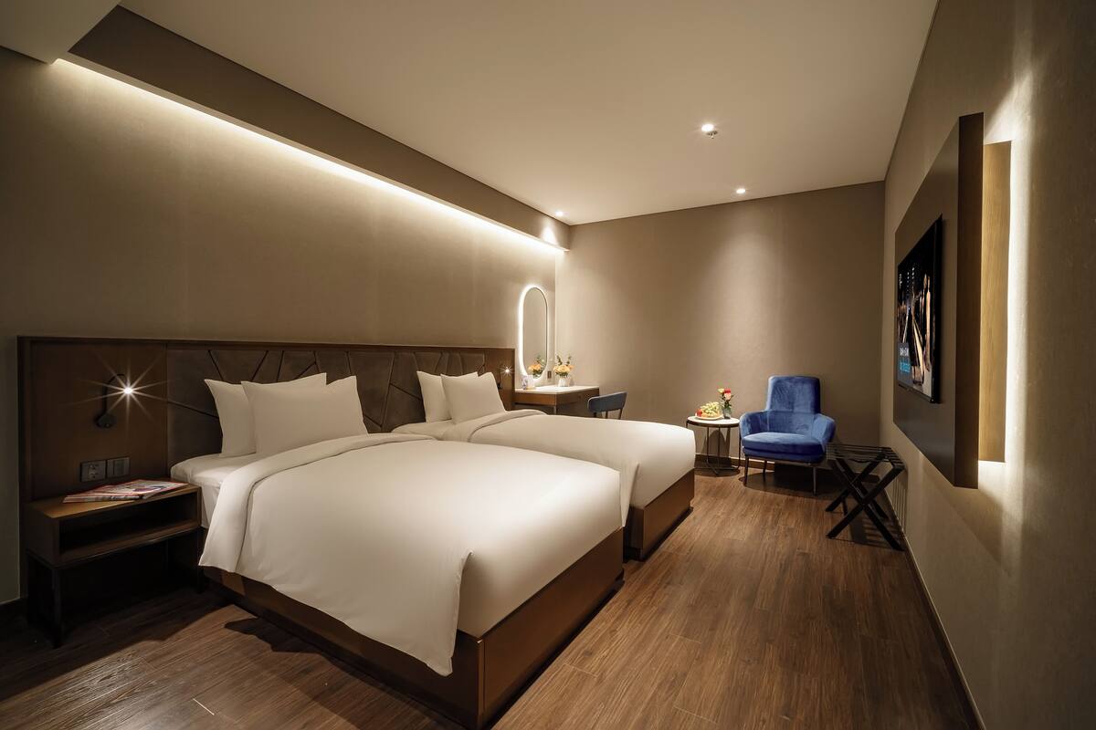 A modern hotel room with two beds, a desk, a chair, and a small table with flowers.