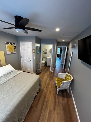 Ein Schlafzimmer mit Bett, Deckenventilator, einer weißen Tür und einem zur Toilette führenden Gang.