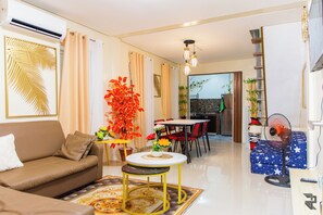 A modern living room with a sofa, a small round table, and a dining area with chairs. There is a fan and a decorative plant in the room. - COZY Up to 16 Guest Near  Aqua Planet & Clark international Speedway (Angeles)