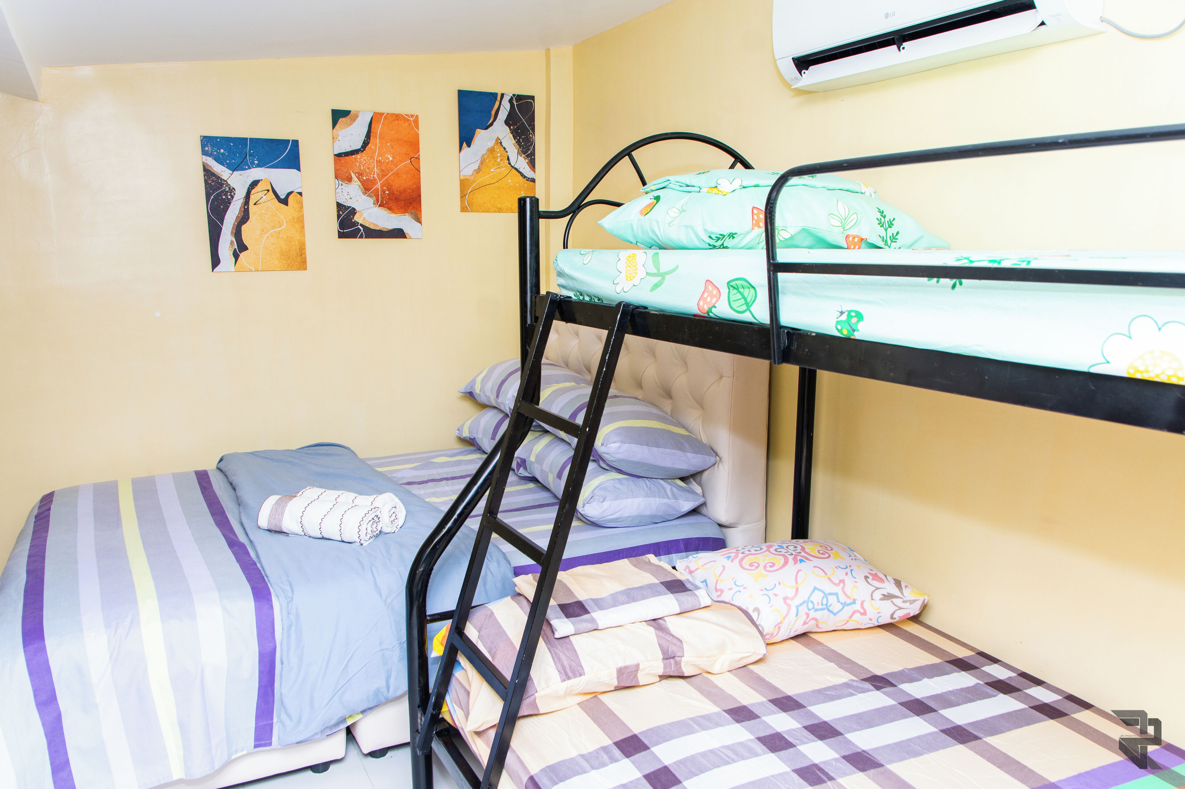 A bunk bed with a striped bedspread, a pillow with a pineapple pattern, and a wall-mounted air conditioner.