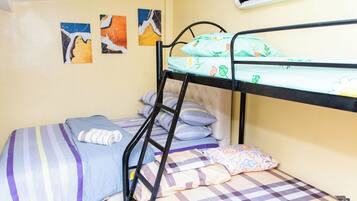 A bunk bed with a striped bedspread, a pillow with a pineapple pattern, and a wall-mounted air conditioner.