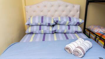 Una cama con cabecera capitonada, almohadas a rayas y una toalla enrollada.