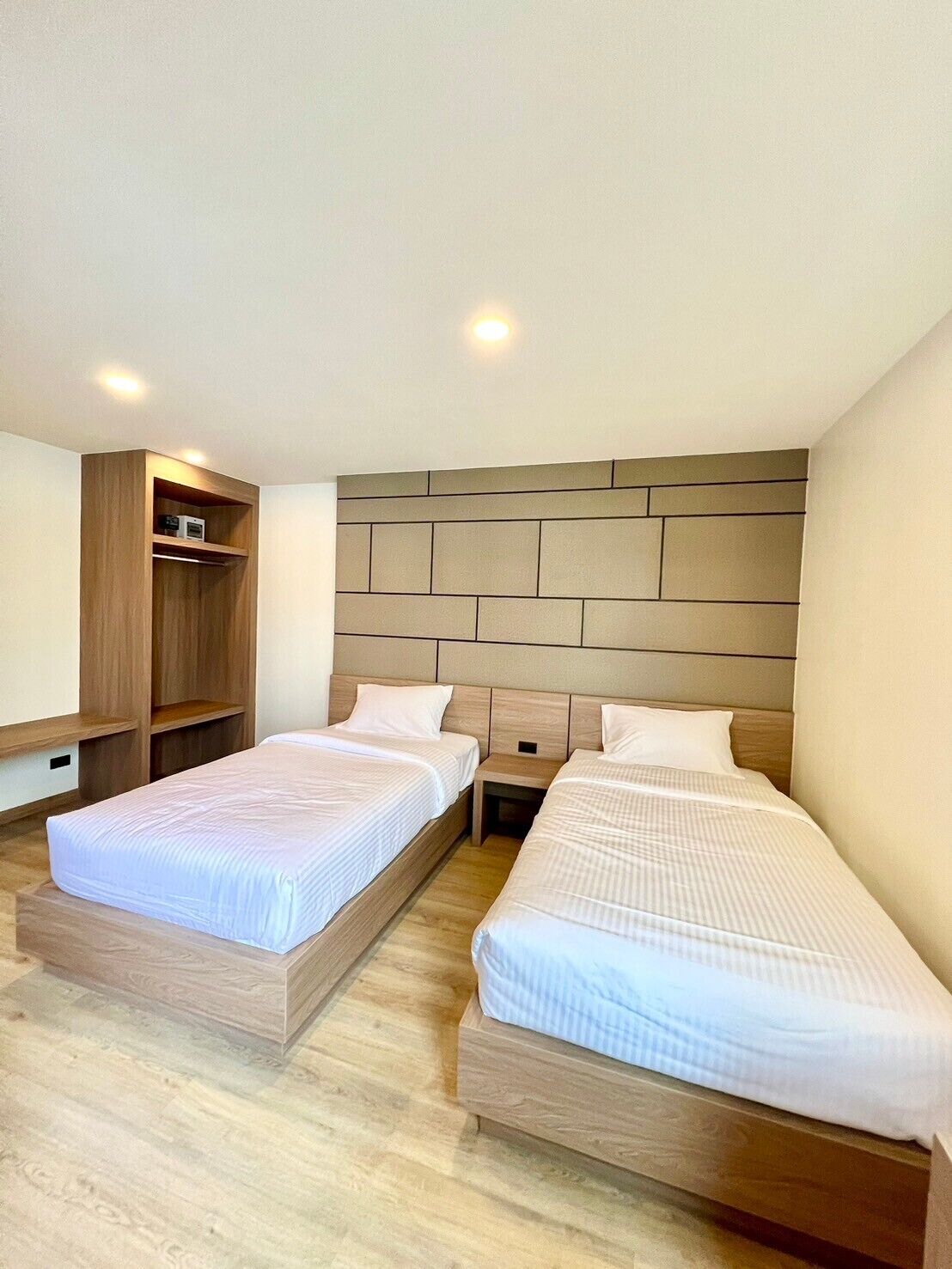 Une chambre d’hôtel moderne avec deux lits simples, une tête de lit en bois et des étagères intégrées.