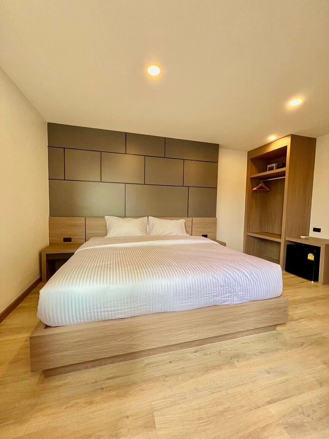 Quarto moderno com cama grande, cabeceira de madeira, mesas de cabeceira e guarda-roupa embutido.