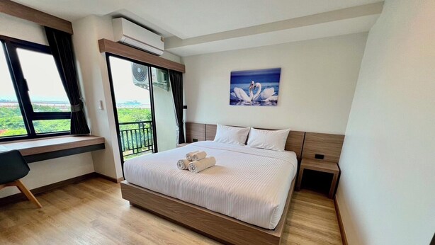 A modern hotel room with a large bed, a desk, and a balcony with a view. - Wellgrow Hotel (Bang Pakong)